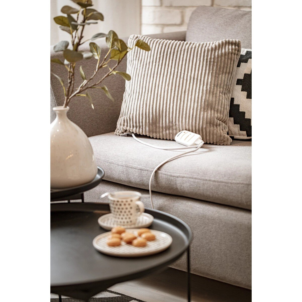 Prążkowana poduszka leży na kanapie obok filiżanki i ciastek na stoliku.