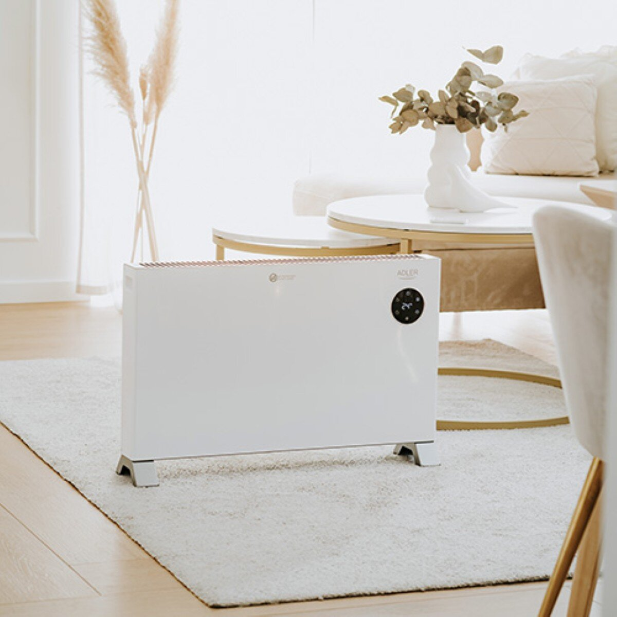 Biały grzejnik na dywanie przed sofą i stolikiem kawowym.