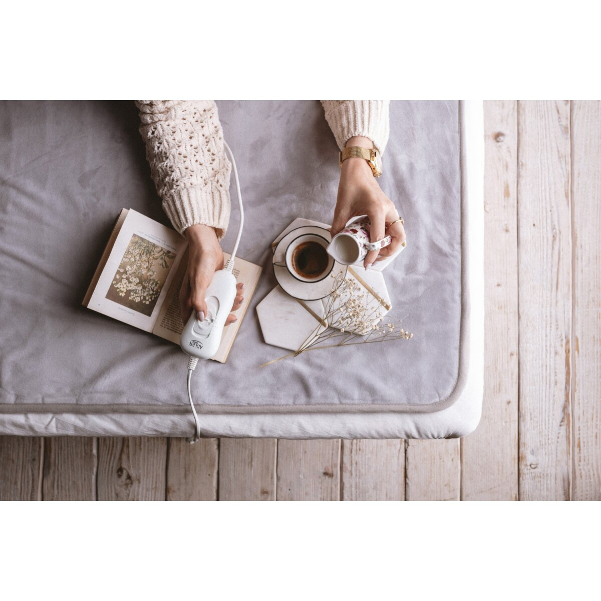 Przytulna scena: Osoba trzymająca kontroler koca elektrycznego, nalewająca mleko do kawy.