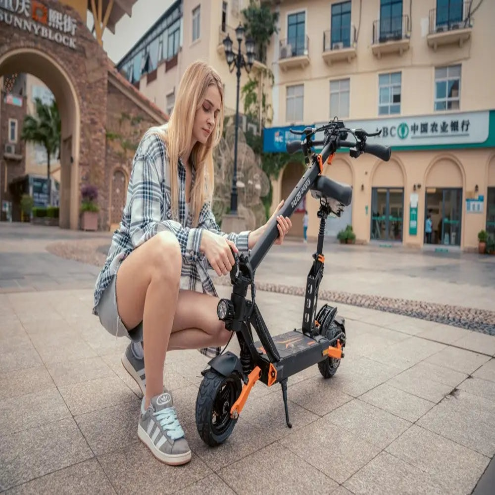 Una mujer rubia con camisa a cuadros se arrodilla junto a un patinete eléctrico negro y naranja.