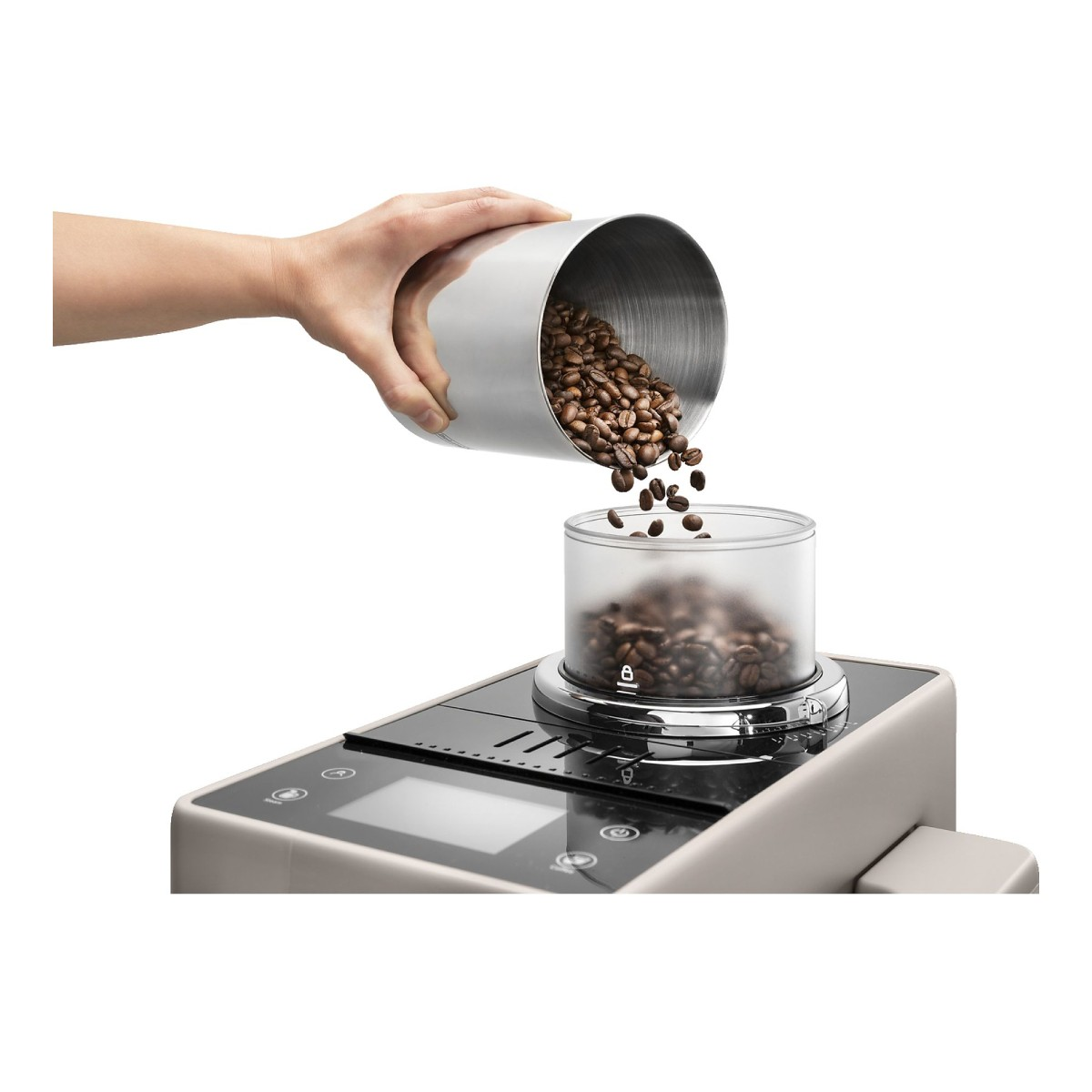 Ręka wsypuje ziarna kawy z metalowego pojemnika do przezroczystego zasobnika młynka.