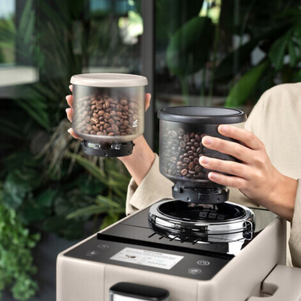 Dłonie trzymają pojemniki z ziarnami kawy nad ekspresem do kawy z ekranem.