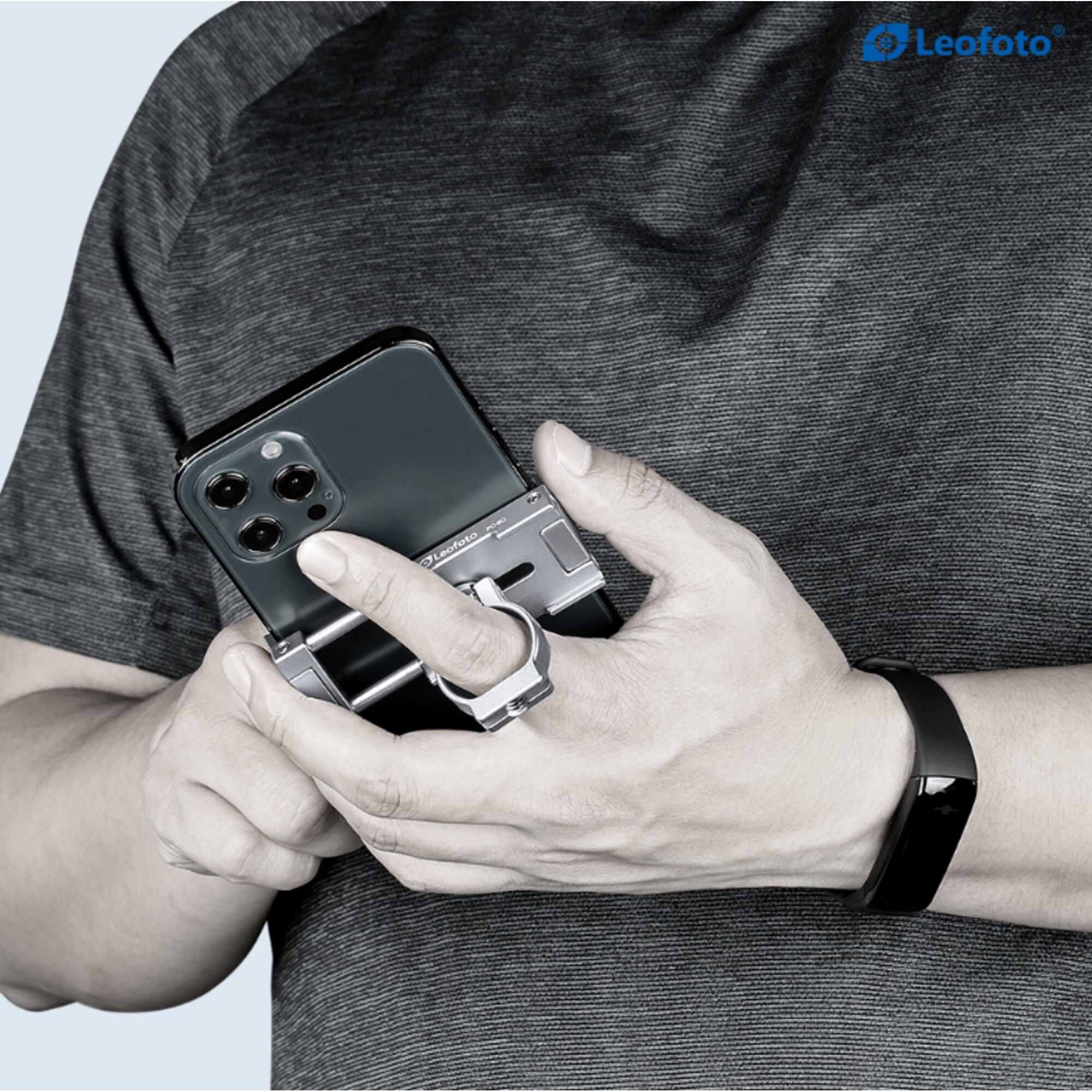 Eine Person trägt ein dunkelgraues Hemd und einen schwarzen Fitness-Tracker. Sie hält ein Smartphone mit silbernem Griff und Ring.