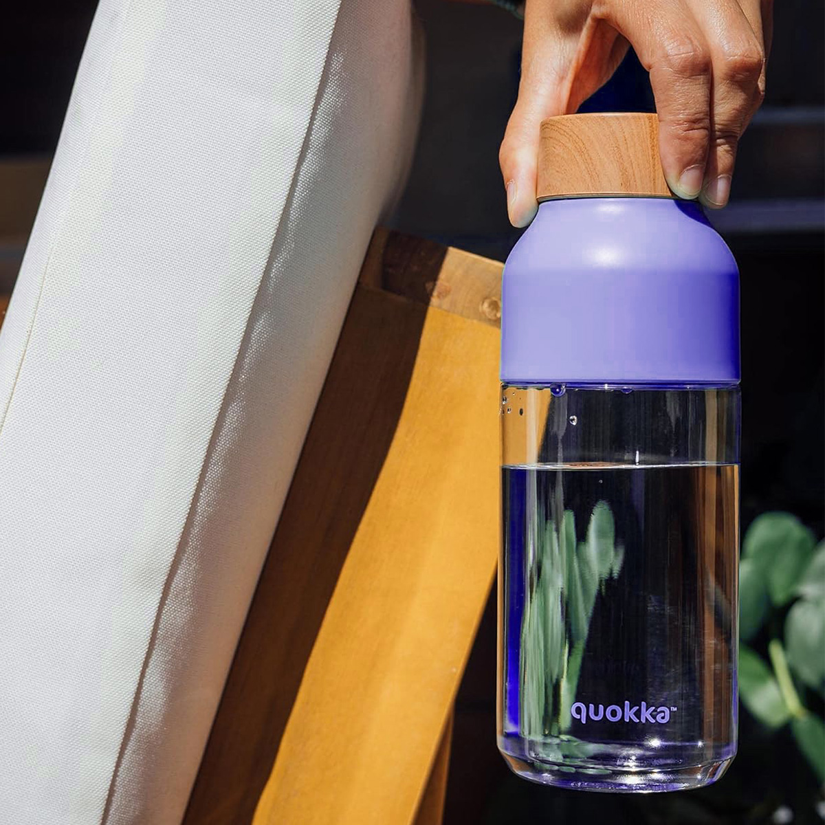 Una persona tiene una bottiglia di vetro trasparente con tappo viola e cima in legno. La bottiglia contiene acqua.