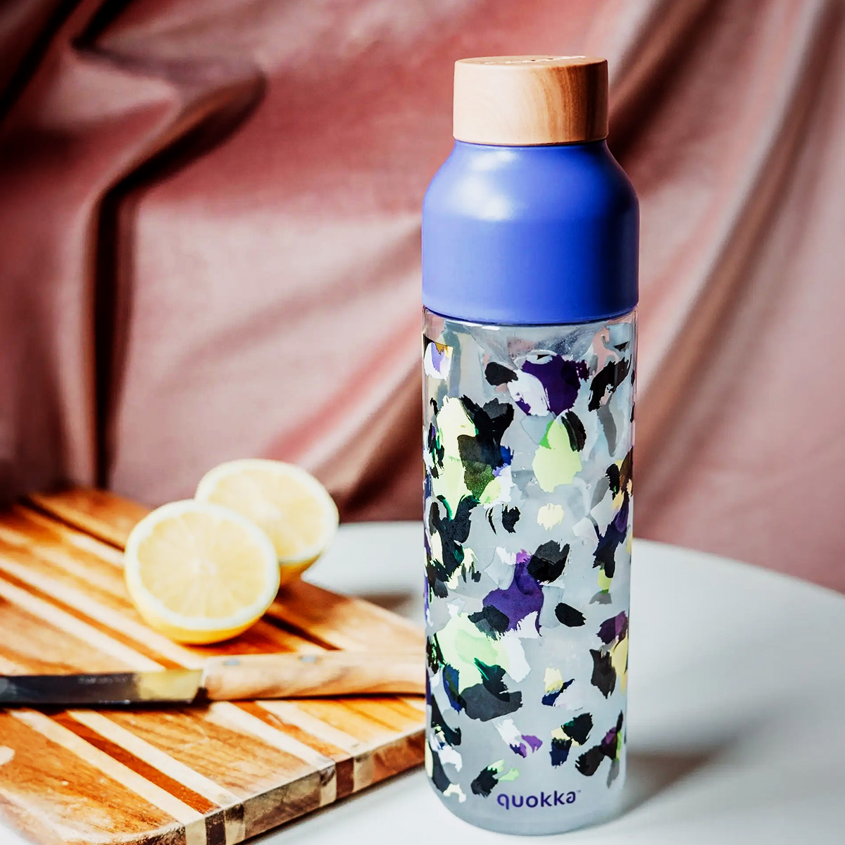 Una botella de agua estampada con tapa azul y parte superior de madera junto a limones.