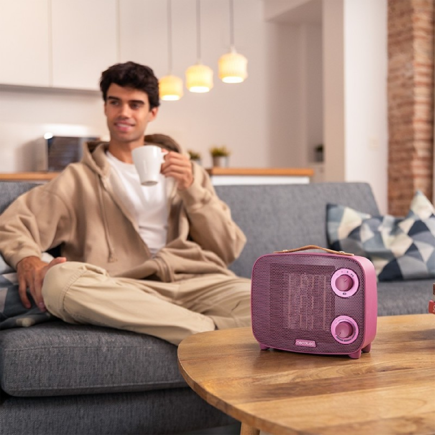 Hombre en sofá con taza, calefactor rosa en mesa. Escena acogedora de sala.