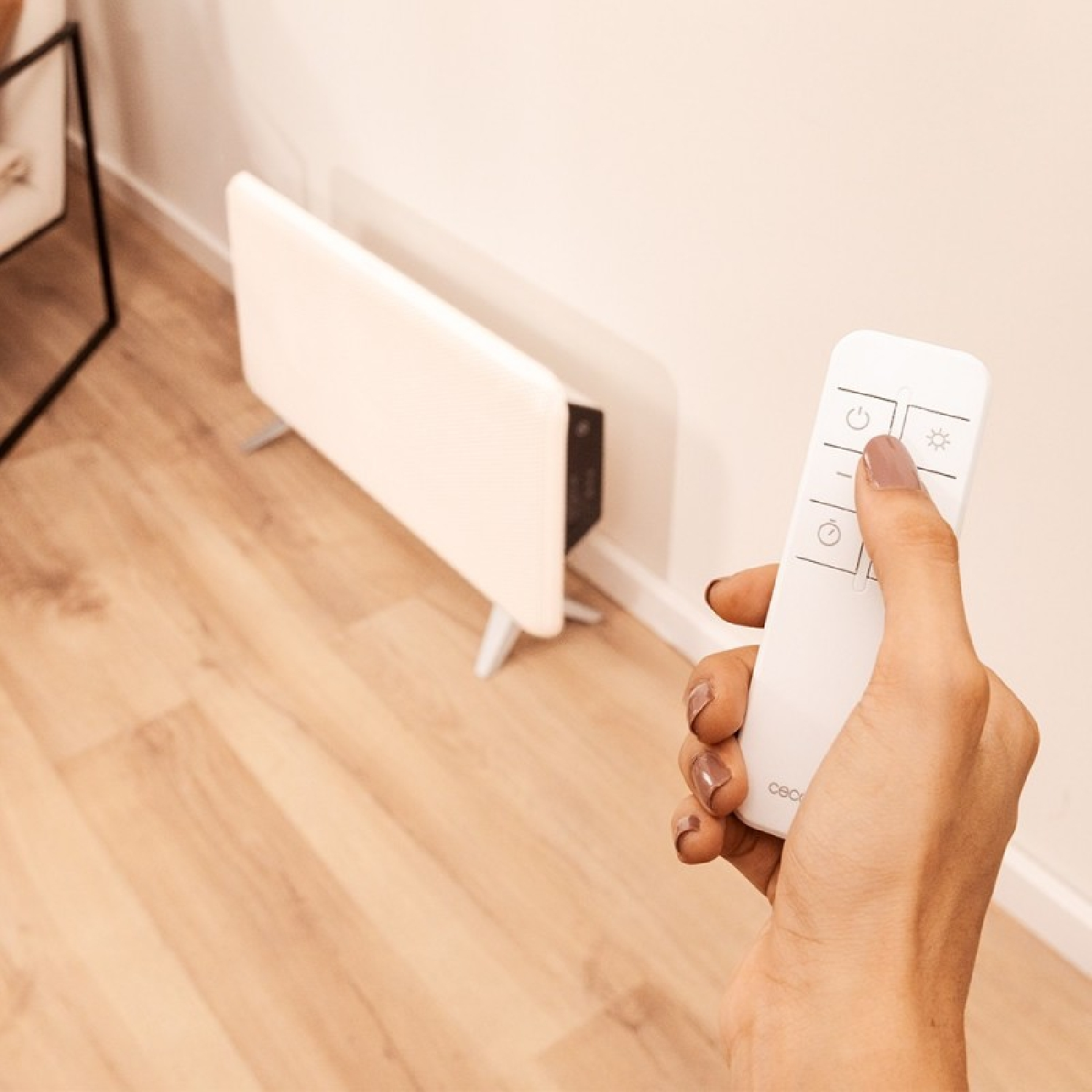 Una mano tiene un telecomando bianco, puntandolo verso un radiatore elettrico bianco.