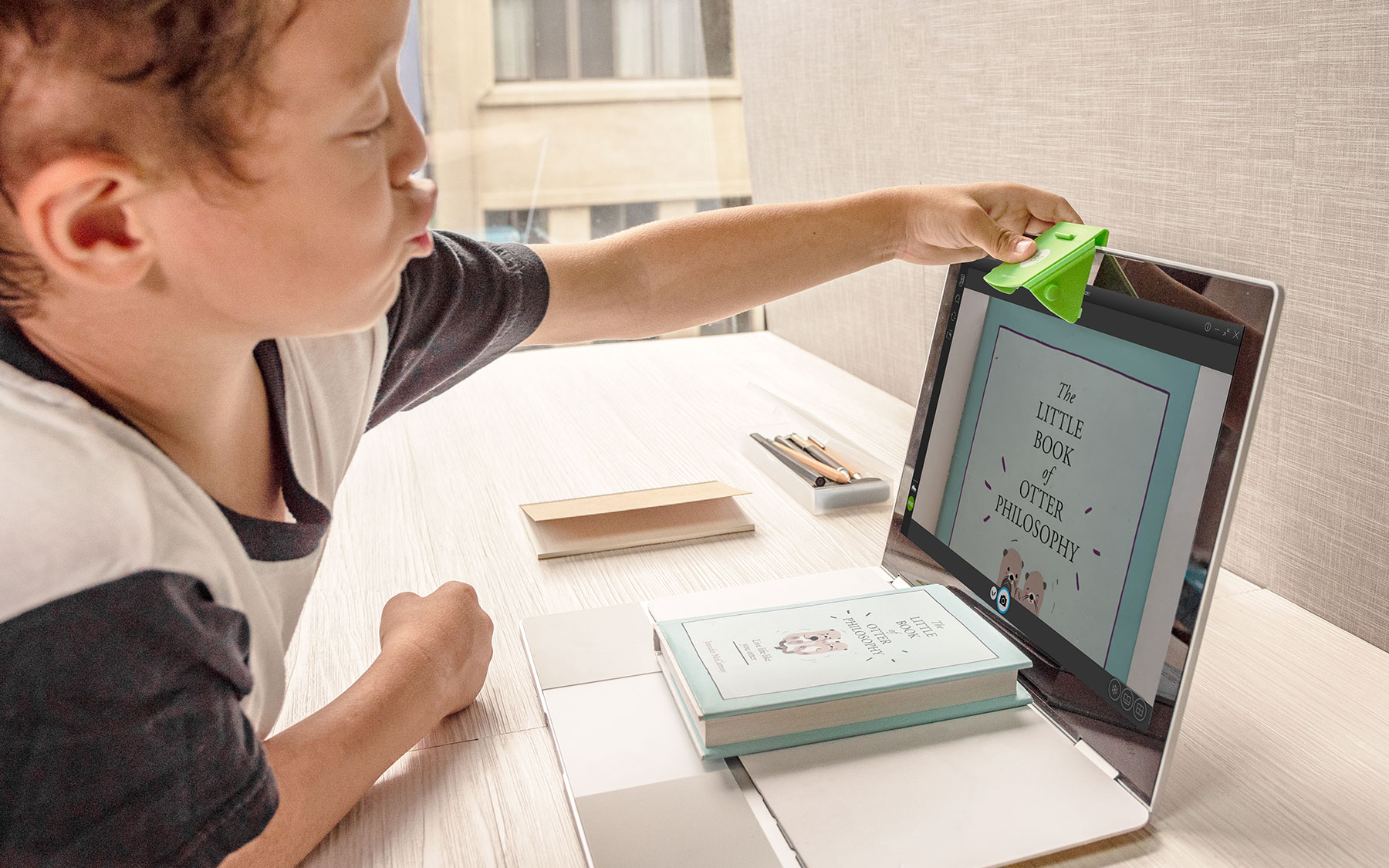 Un ragazzo usa una clip verde per tenere aperto un libro sullo schermo di un laptop.