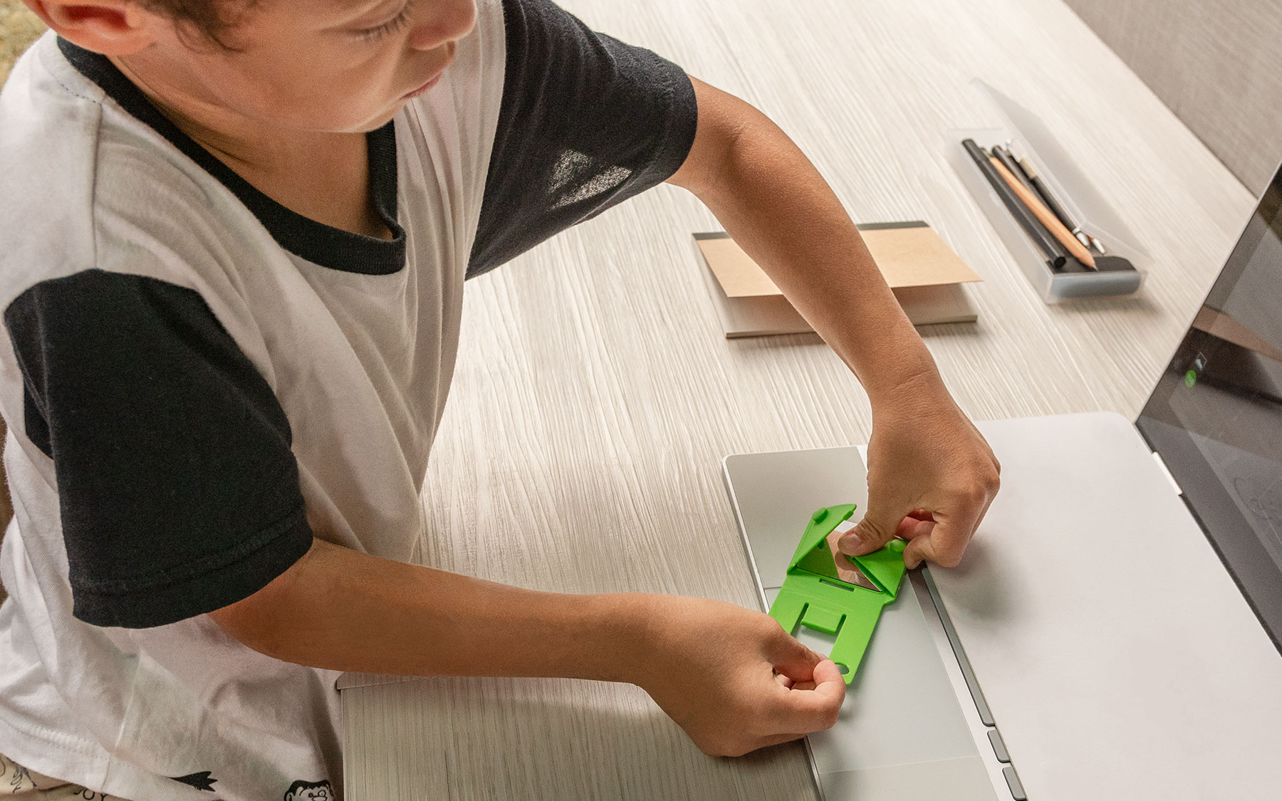 Un bambino sta montando un supporto per telefono verde su un laptop su una scrivania di legno.