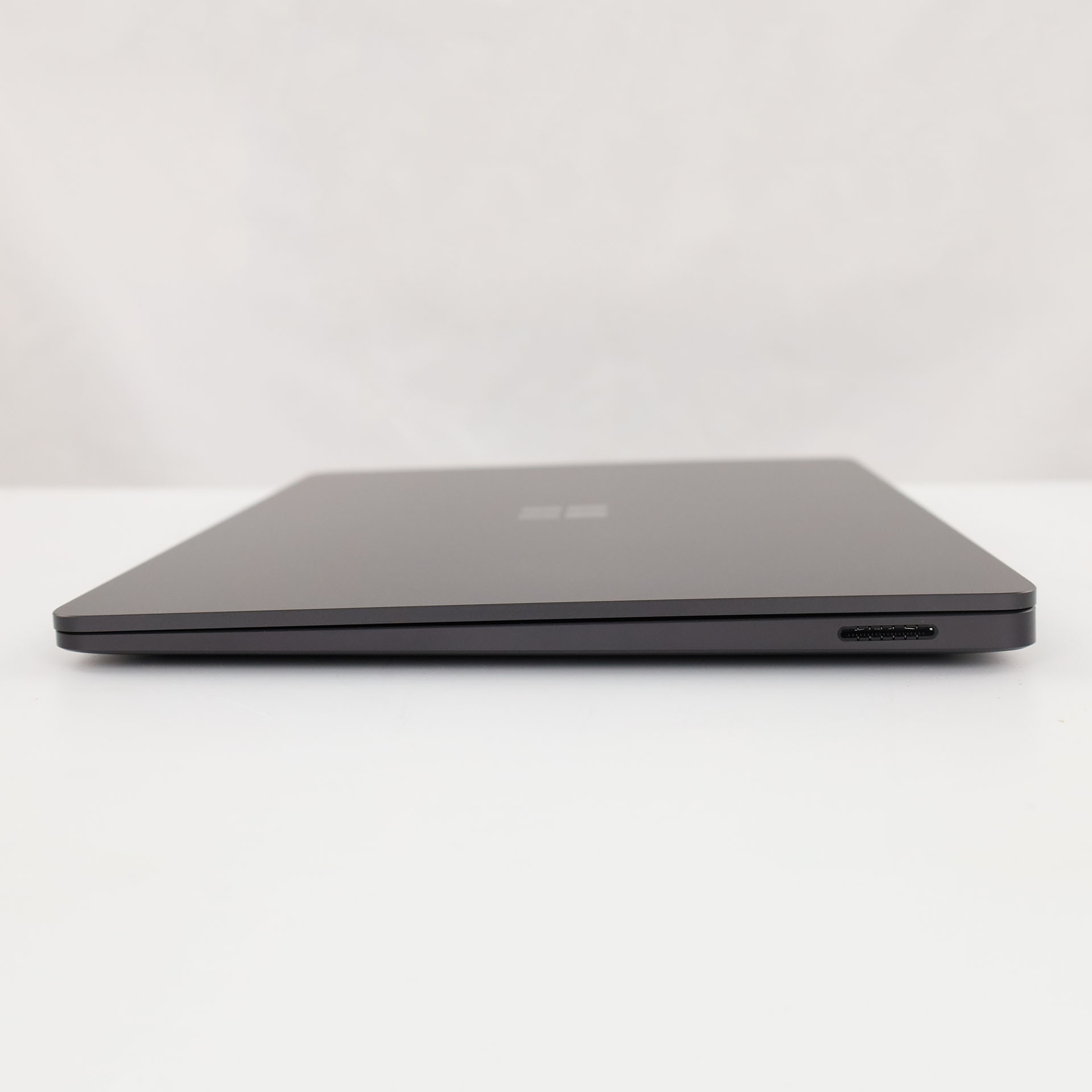 Ein geschlossener, dunkelgrauer Laptop mit einem USB-C-Anschluss an der Seite, auf weißer Oberfläche.