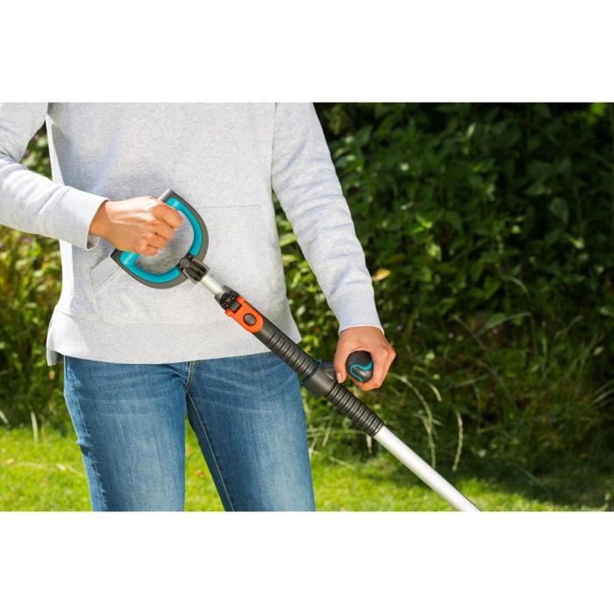 Persona con felpa grigia e jeans blu tiene attrezzo da giardino con manico turchese e nero.