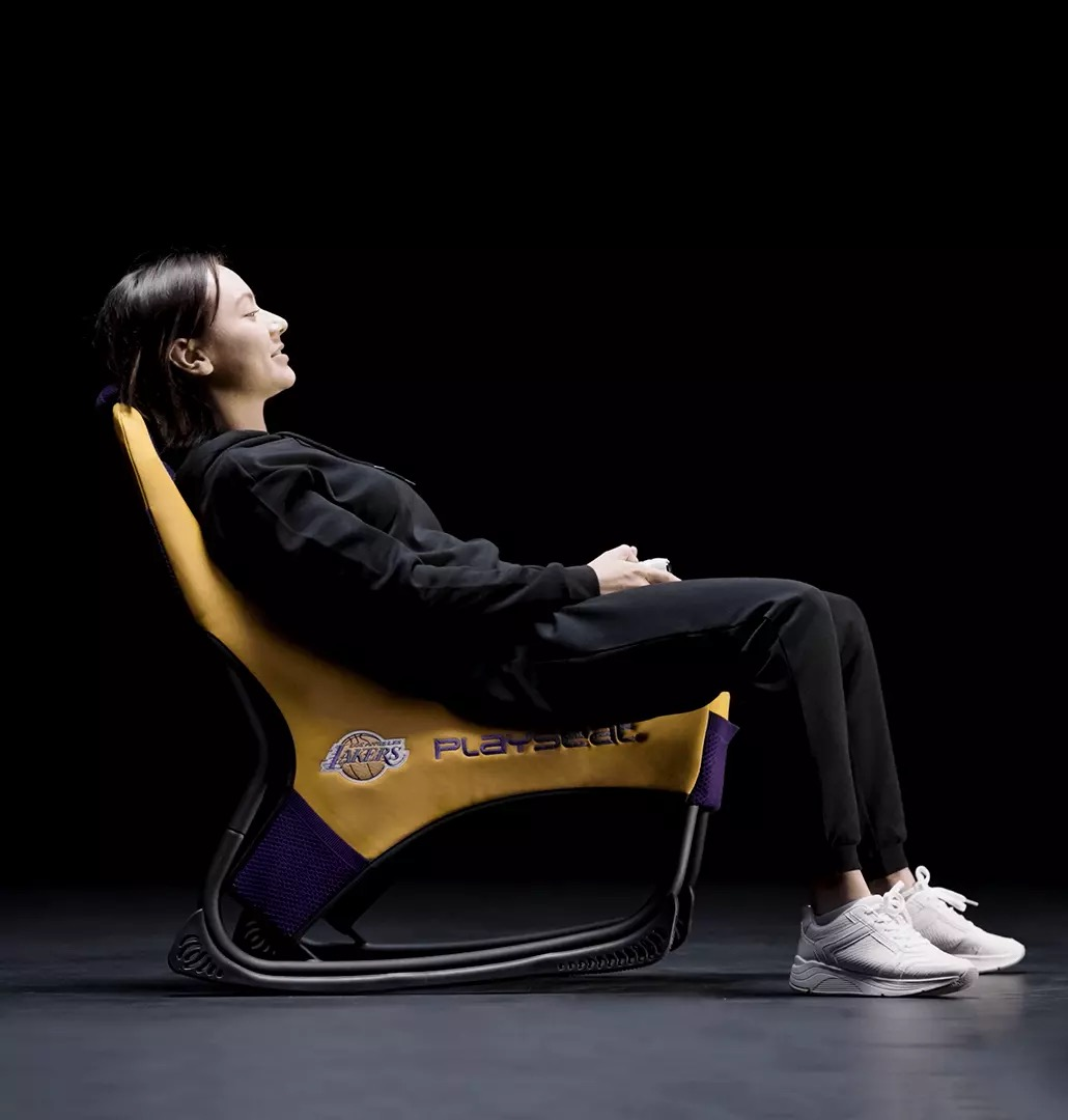 Una donna si rilassa su una sedia Playseat gialla dei Los Angeles Lakers su sfondo nero.
