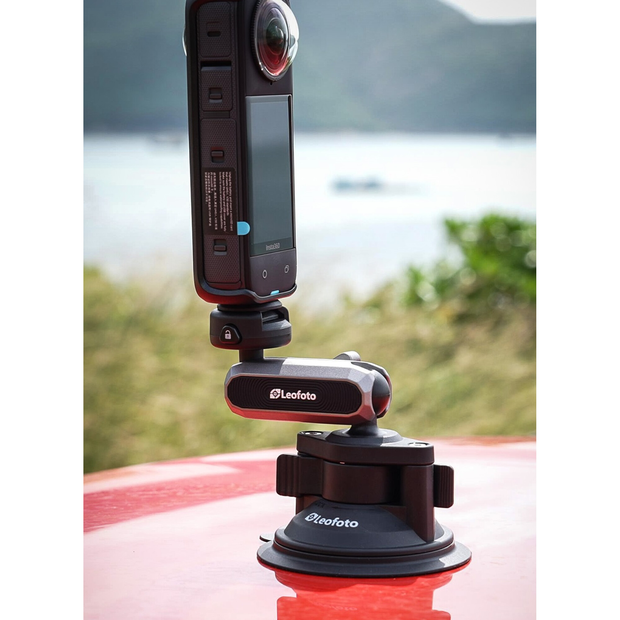 Insta360-Kamera auf einem Leofoto-Saugnapfhalter auf roter Oberfläche, mit unscharfem Hintergrund.