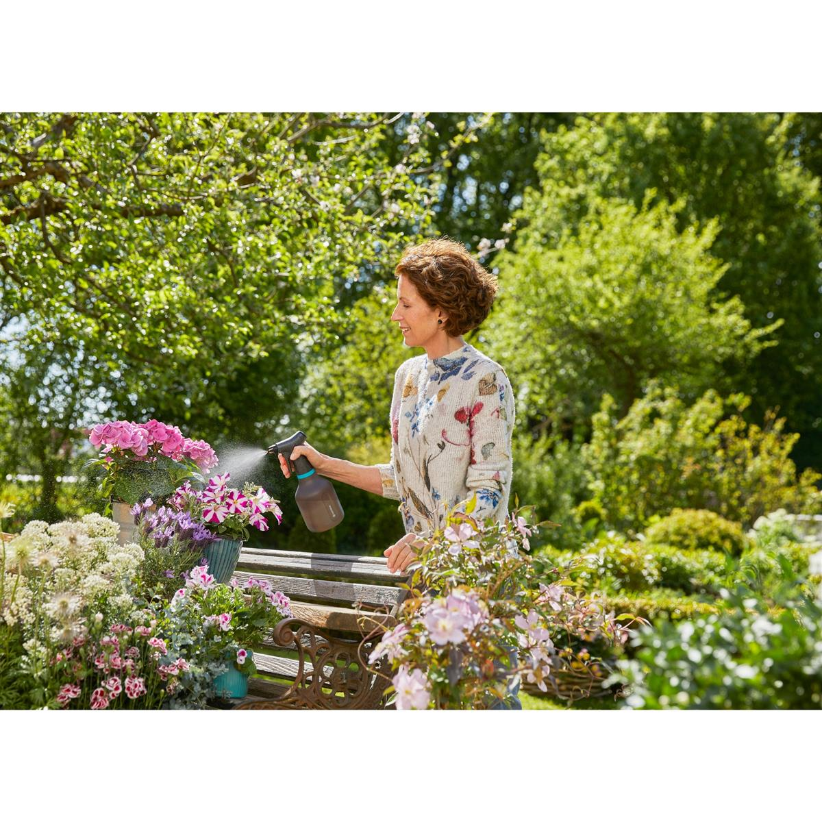 Una donna spruzza fiori in un giardino con uno spruzzino.