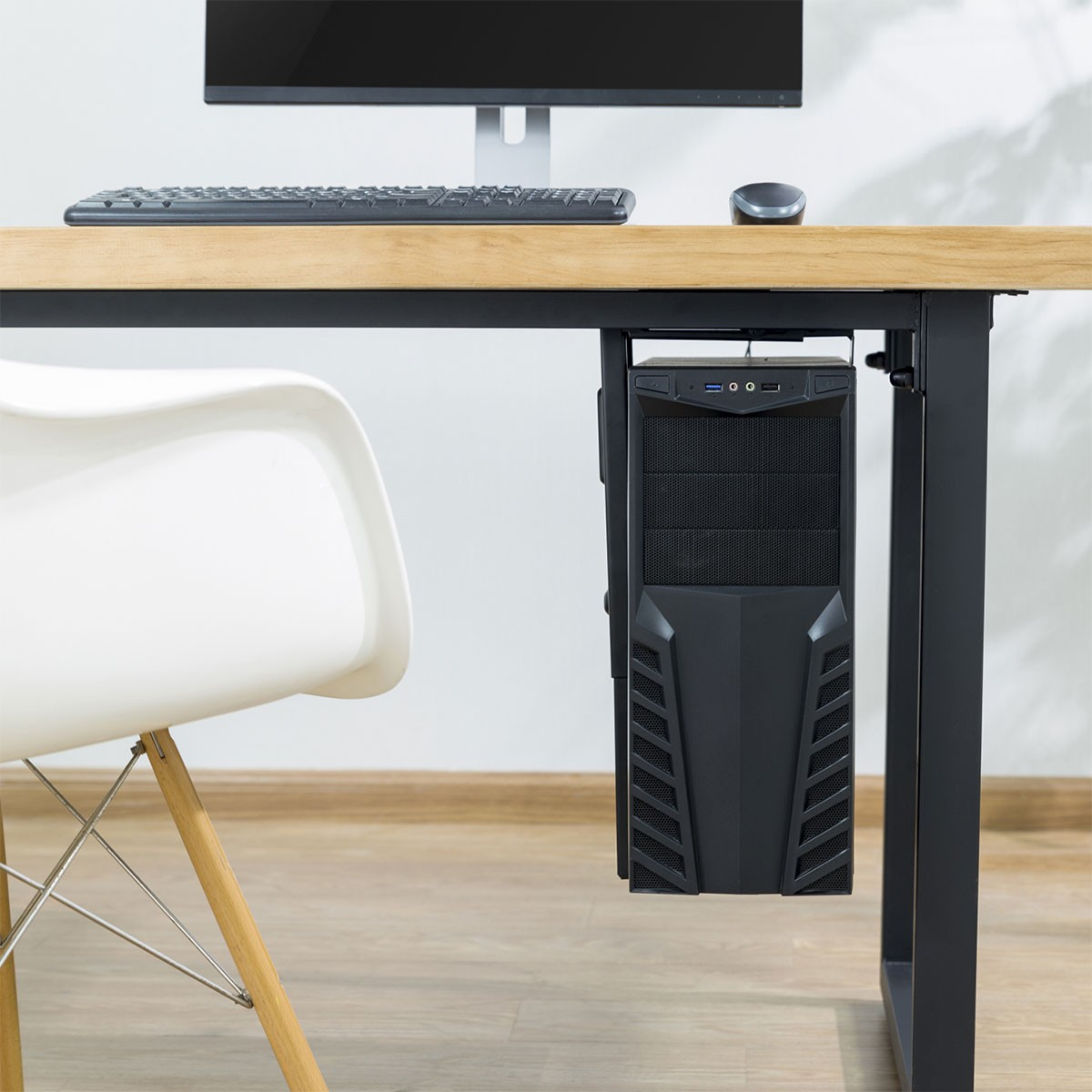 Una tower del computer nera pende sotto una scrivania di legno, accanto a una sedia bianca.