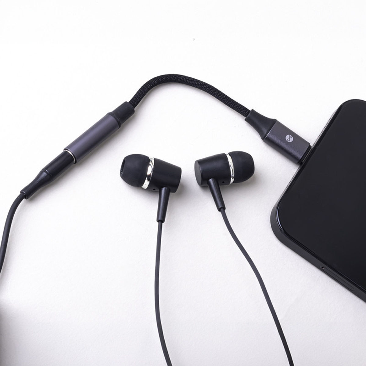 Auricolari neri con cavo intrecciato collegati a uno smartphone nero su sfondo bianco.