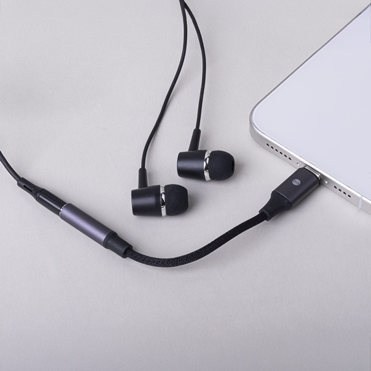 Auricolari neri con anello argentato collegati a uno smartphone tramite adattatore USB-C.