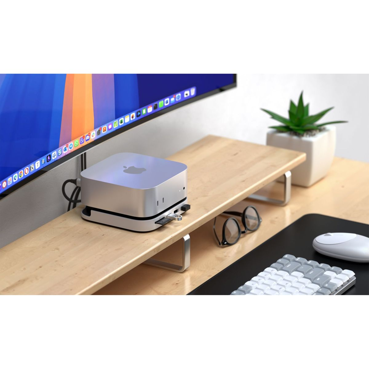 Ein silberner Apple Mac Studio steht auf einem Holzständer mit Monitor, Tastatur, Maus und Brille.