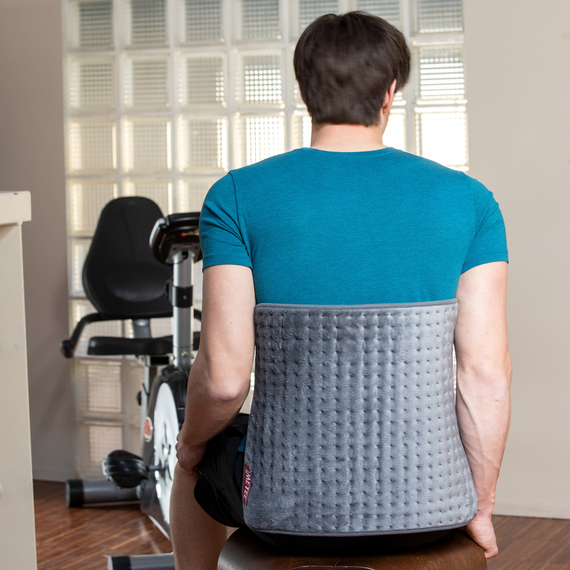 Hombre con corsé lumbar sentado en taburete, bicicleta estática detrás.