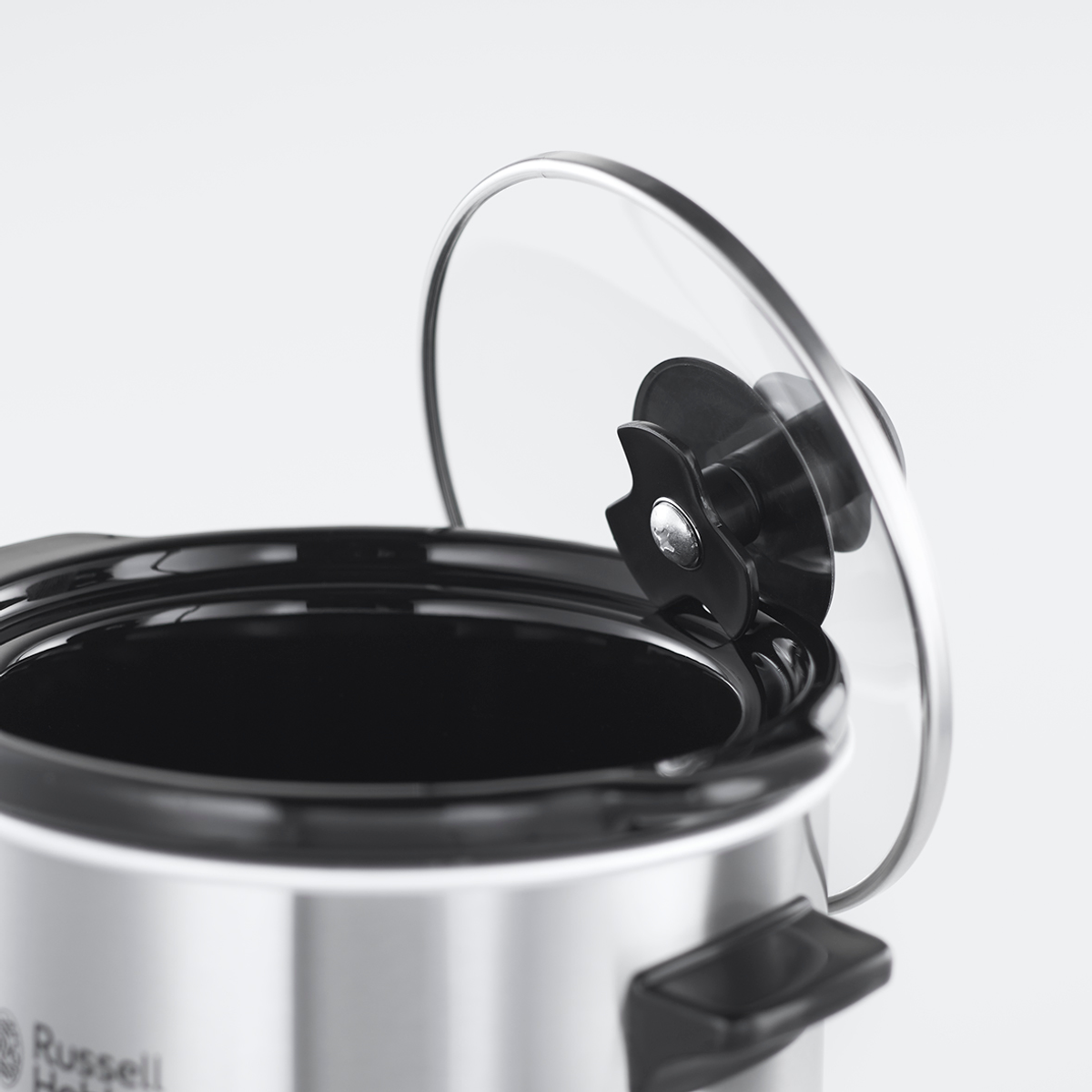 Primo piano di una slow cooker argentata con coperchio in vetro parzialmente aperto.