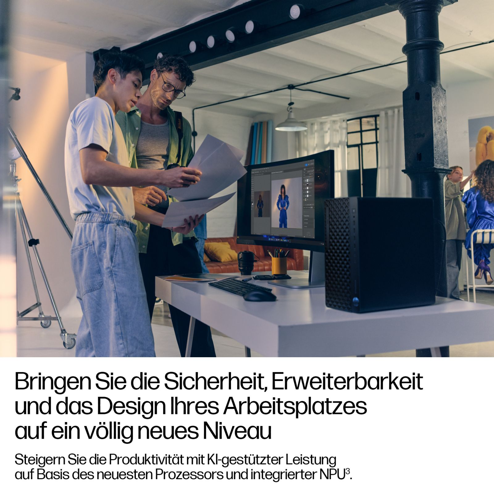 Zwei Männer prüfen Papiere vor einem Computer in einem Büro mit Studiobeleuchtung.