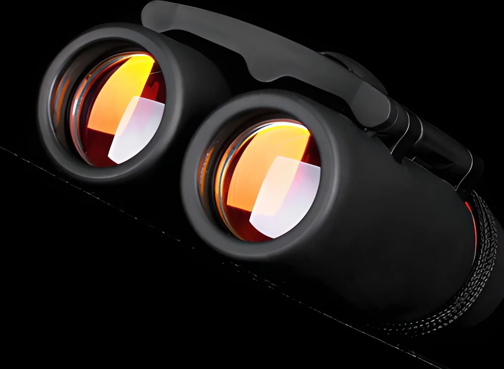 Nahaufnahme einer schwarzen Fernglas mit orange getönten Linsen vor schwarzem Hintergrund.