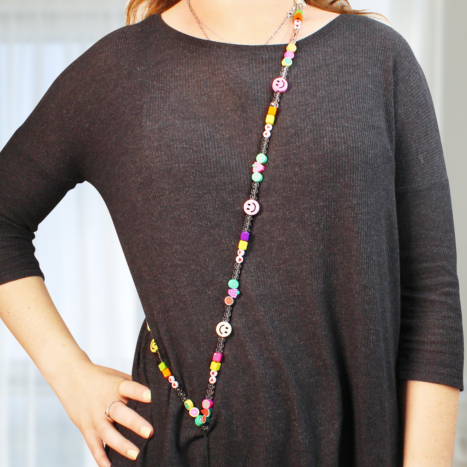 Donna con maglia scura indossa una collana di perline colorata con faccine sorridenti e ciondoli di frutta.
