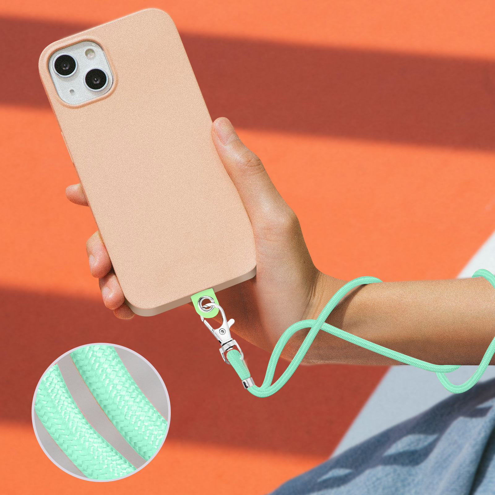 Una mano tiene un iPhone color pesca con un laccetto verde menta attaccato alla custodia.