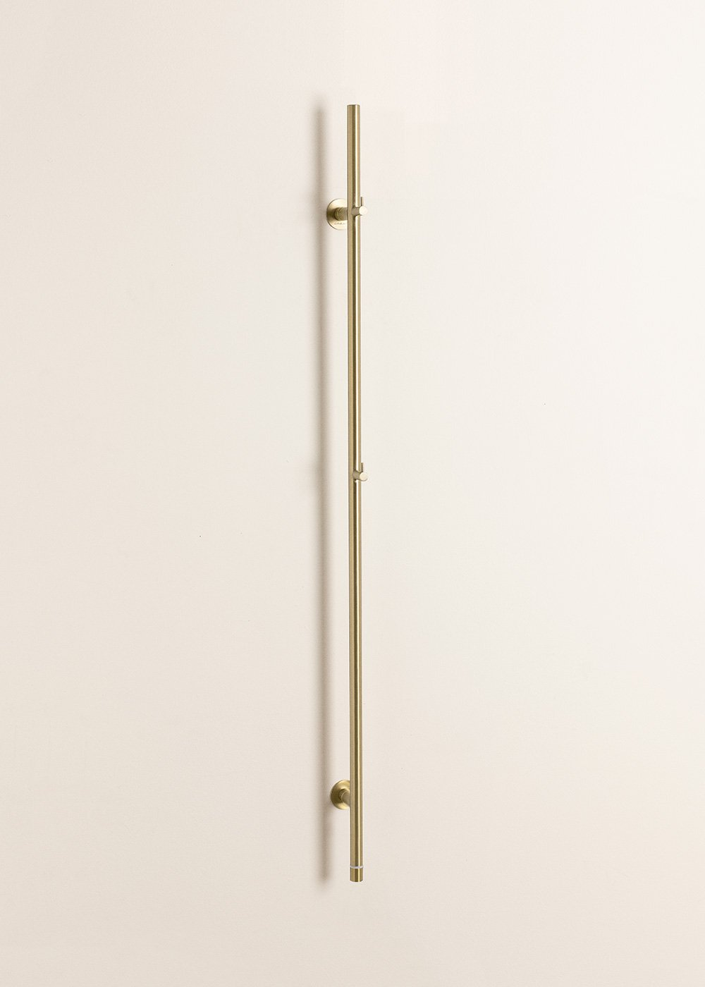 Un tirador de puerta largo, delgado y de latón montado verticalmente en una pared color crema.