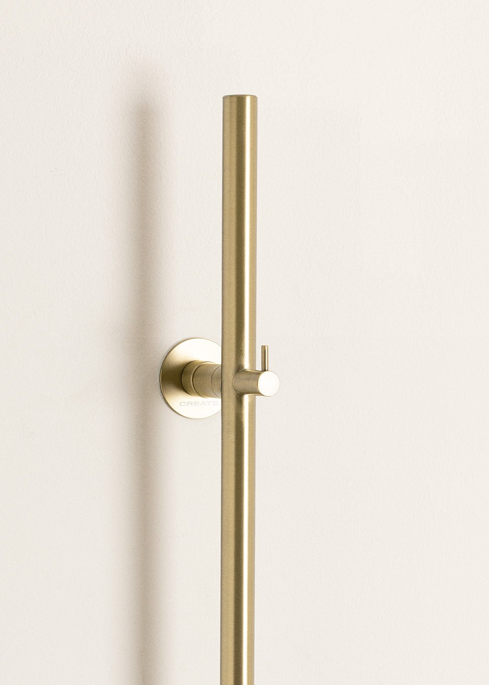 Un soporte dorado para alcachofa de ducha en pared blanca.
