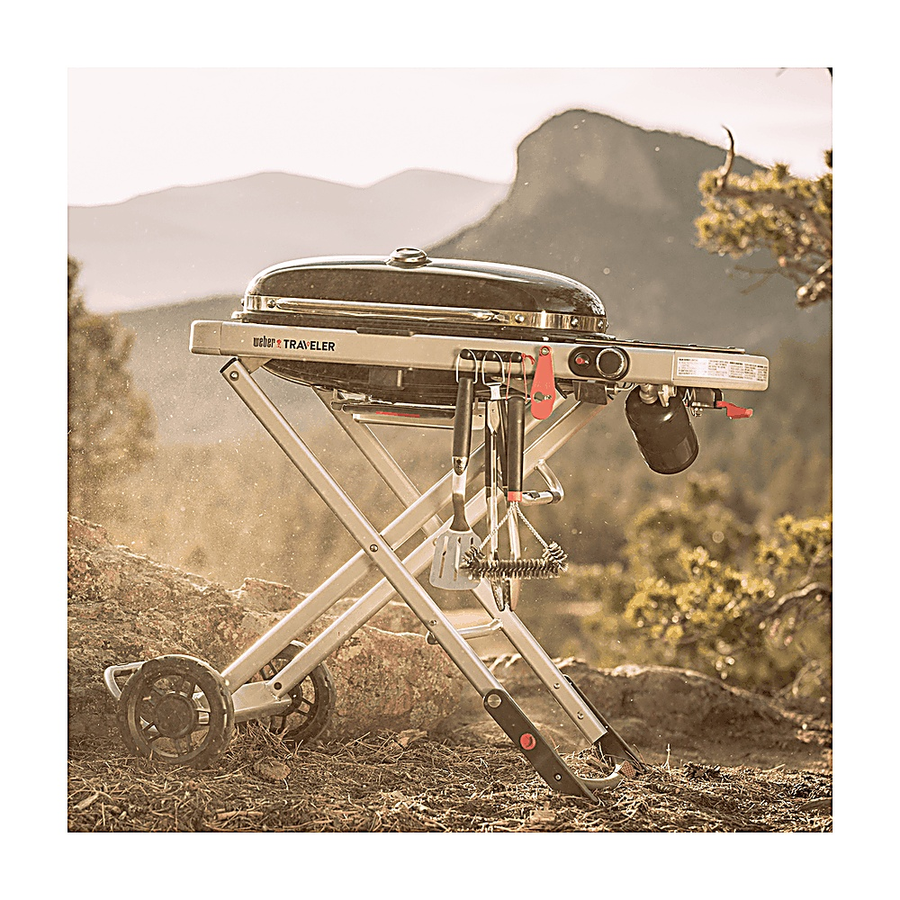 Przenośny grill Weber Traveler stoi na skalistej powierzchni z górami w tle.