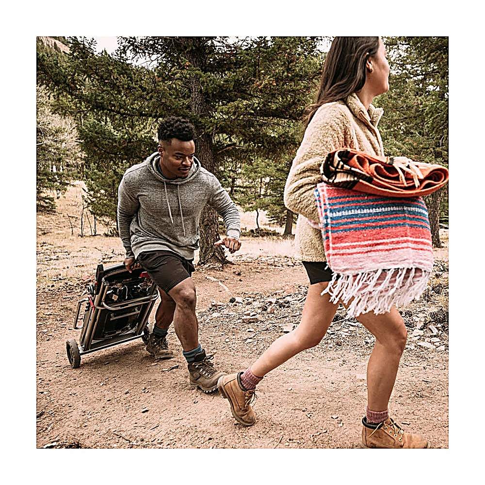 Mężczyzna ciągnie wózek, kobieta niesie koce. Idą leśną ścieżką.