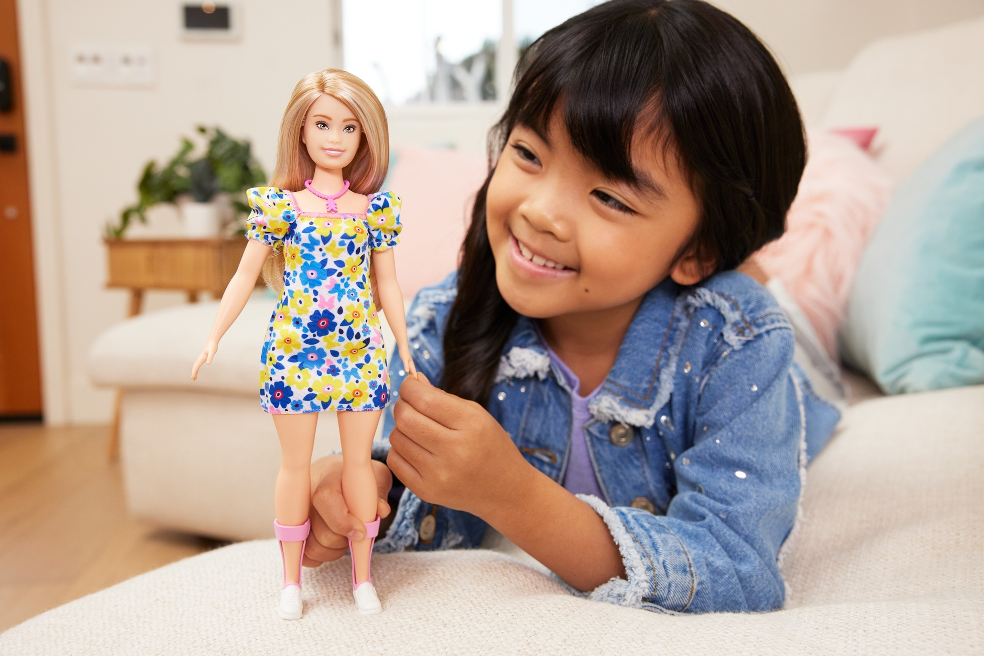 Ein lächelndes Mädchen in einer Jeansjacke hält eine Barbie-Puppe in einem Blumenkleid.