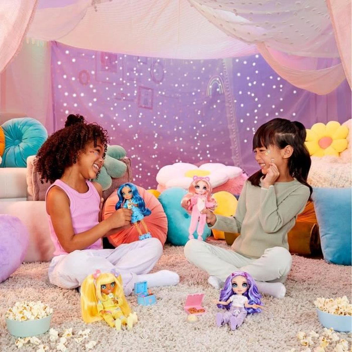 Due bambine giocano con bambole in una tenda decorata con luci stellate. Popcorn sparso.