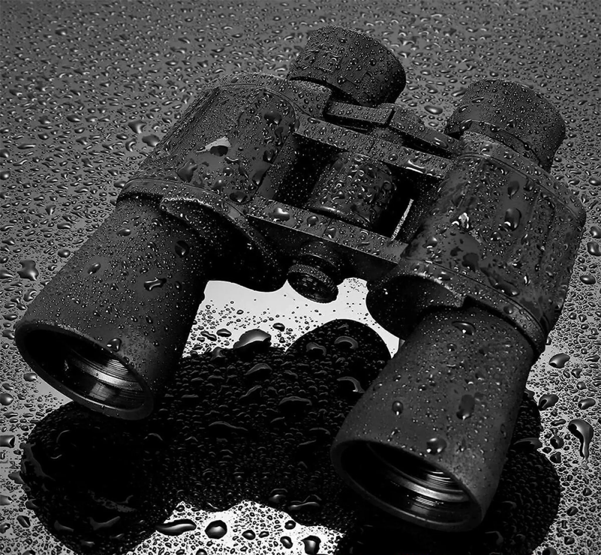 Ein schwarzes Fernglas mit Wassertropfen bedeckt liegt auf einer nassen, reflektierenden Oberfläche.