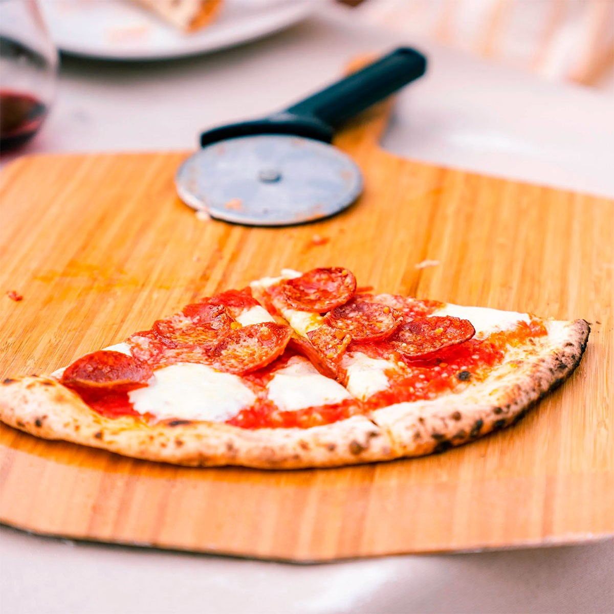 Una fetta di pizza al salame con formaggio fuso su una pala di legno, rotella per pizza vicina.