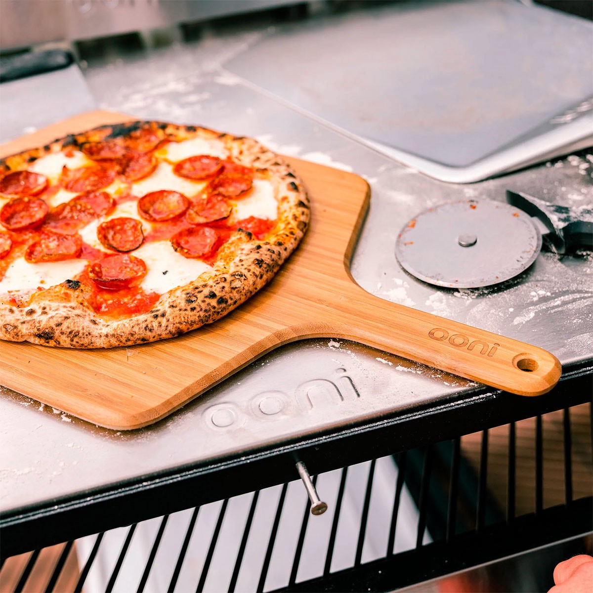 Una pizza al salame piccante riposa su una pala di legno accanto a una rotella per pizza.