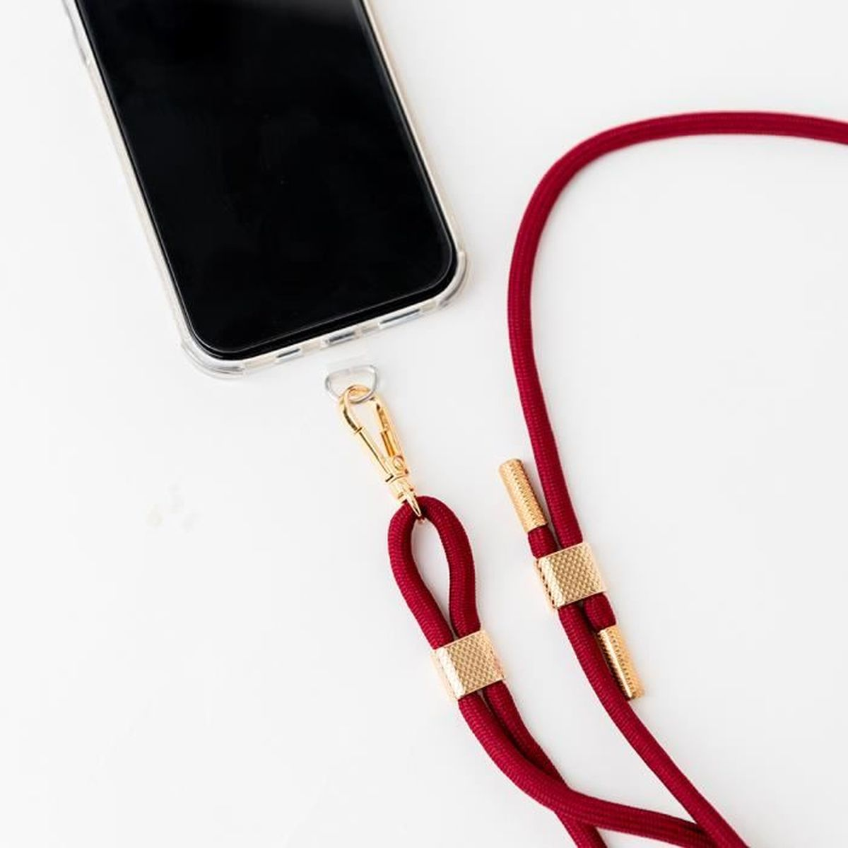 Un cordino rosso con finiture dorate è attaccato a un telefono.