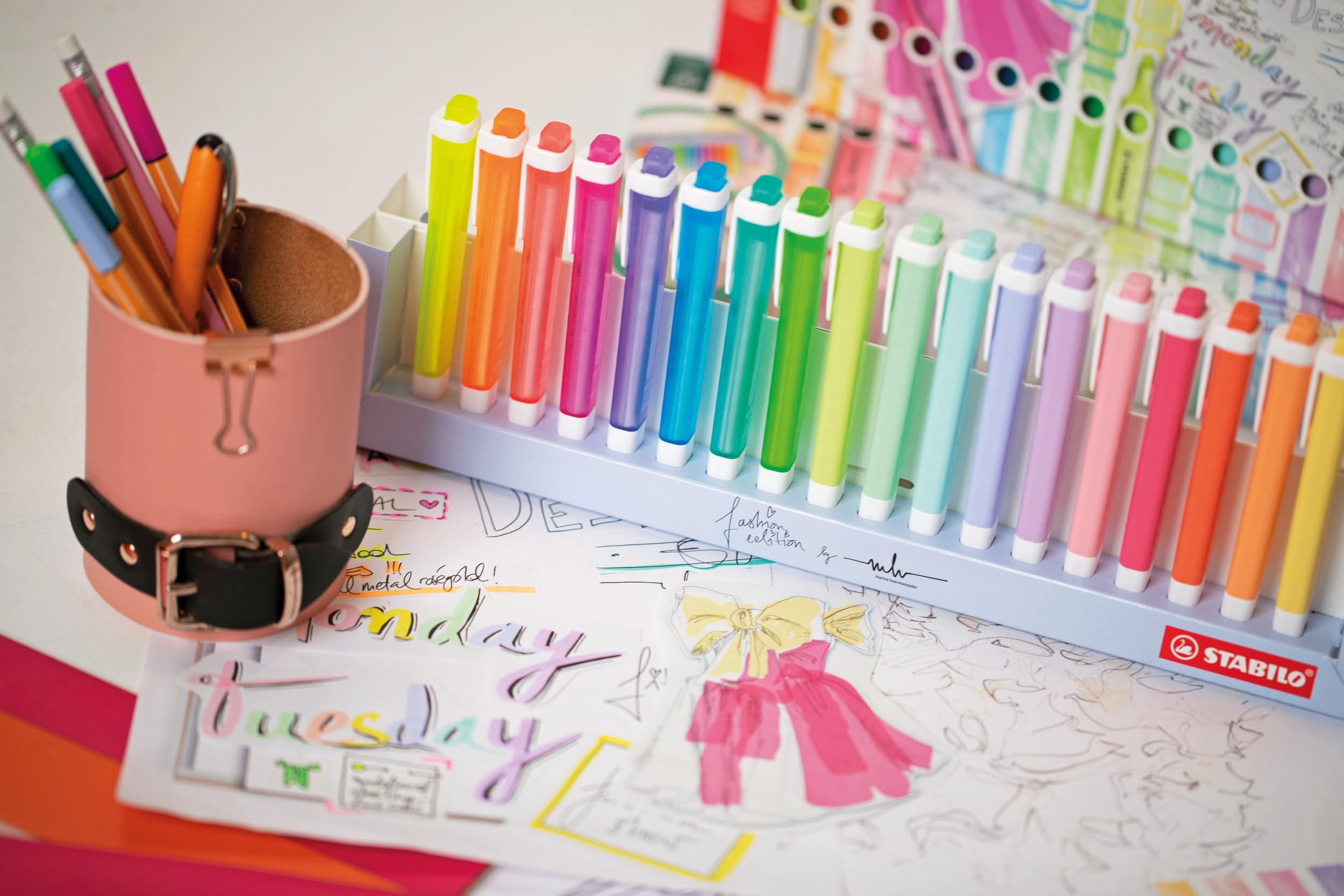 Un portapenne rosa con penne, un vassoio di penne Stabilo colorate e pagine di agenda.