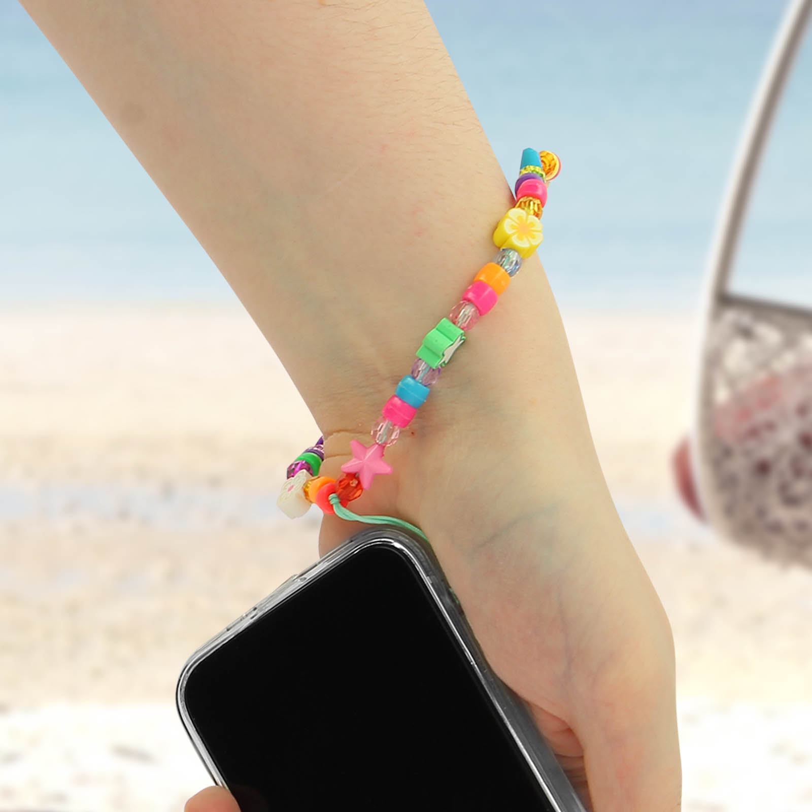 Un braccialetto colorato di perline su un polso che tiene un telefono. Sfondo spiaggia.