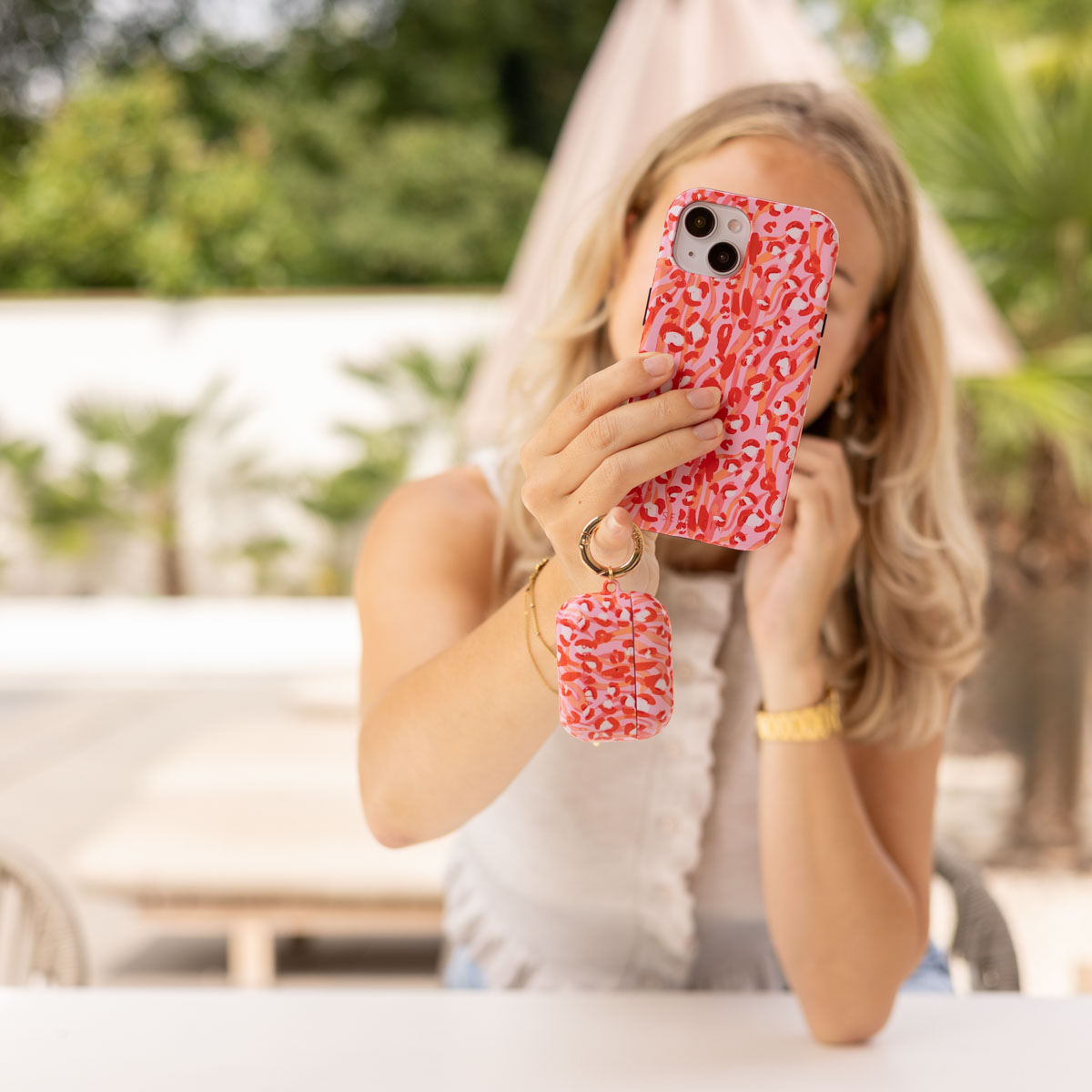 Una mujer sostiene un teléfono rosa con estampado de leopardo y funda AirPod a juego. Al aire libre.