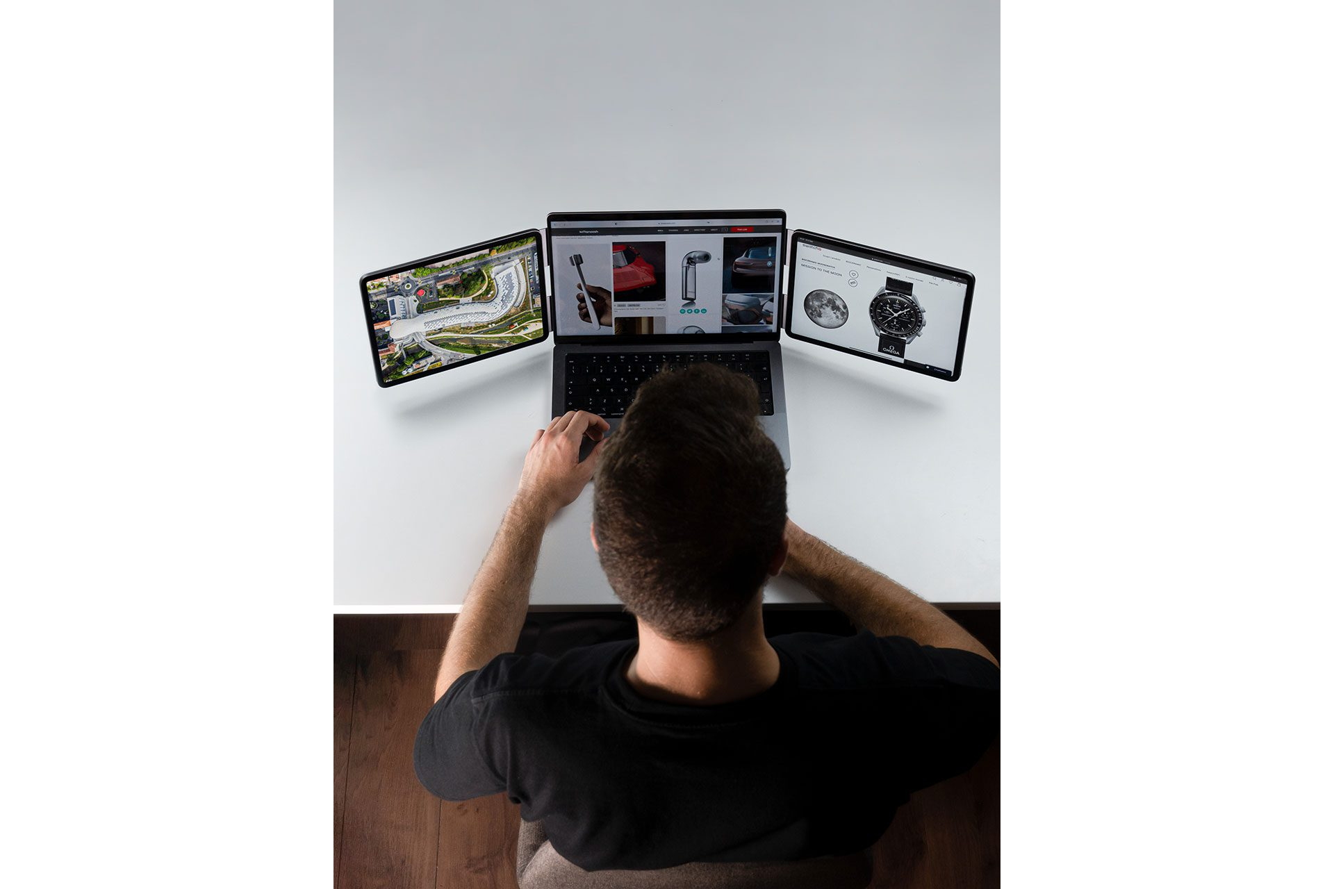 Uomo con maglia scura usa laptop con due tablet laterali che mostrano siti web.