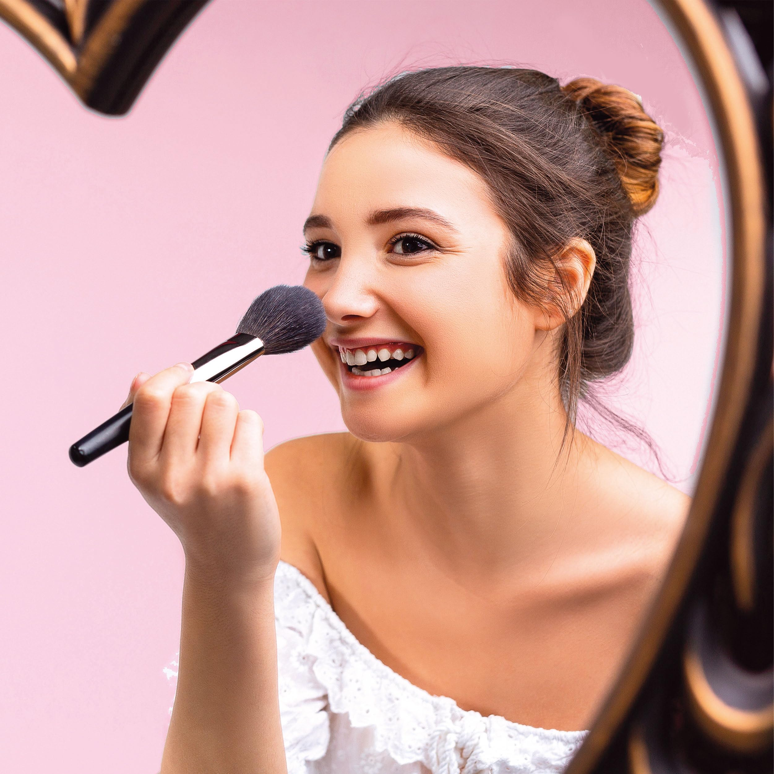 Una donna con i capelli raccolti si applica il trucco sul viso con un pennello.