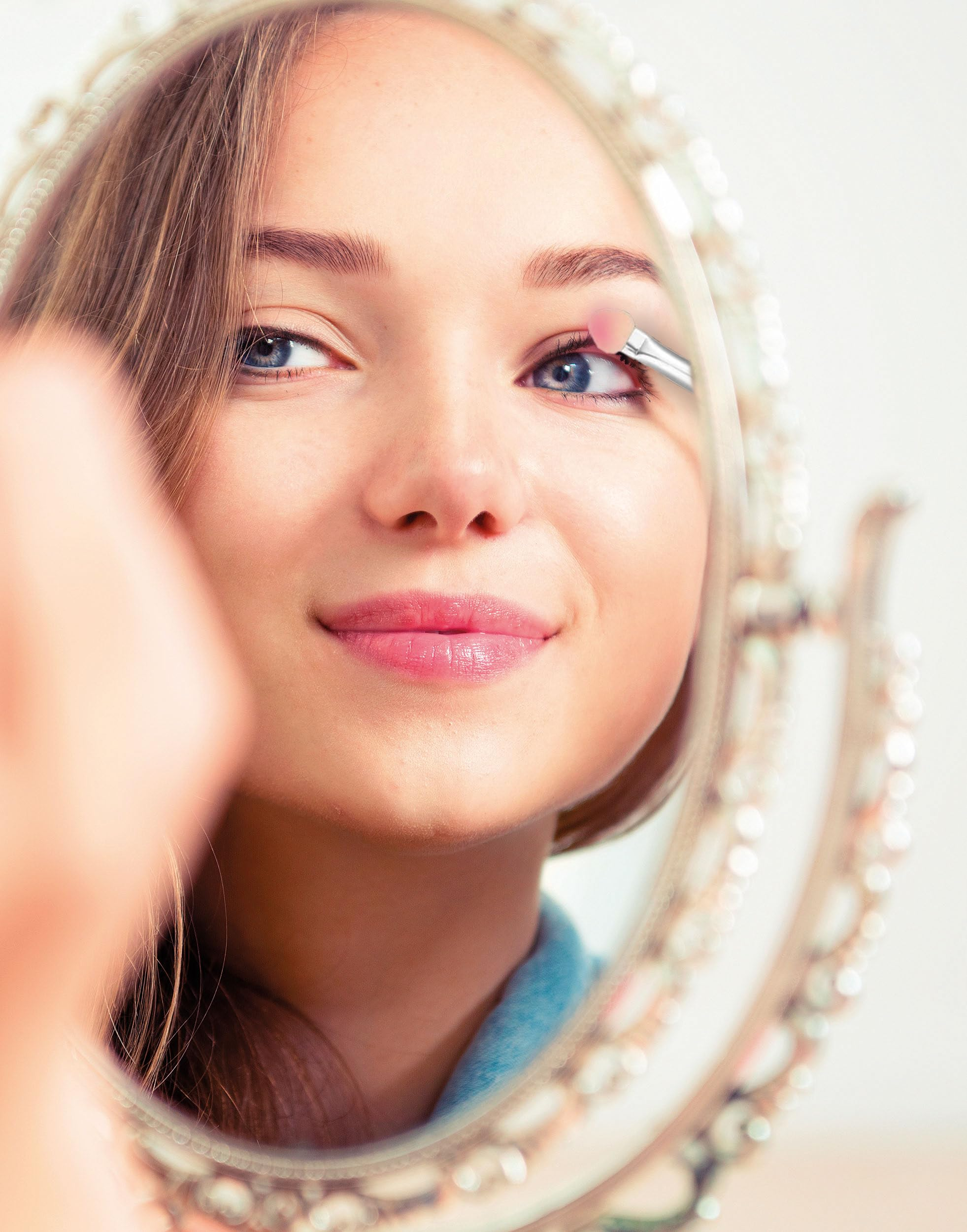 Una giovane donna si applica l'ombretto con un pennello, guardandosi in uno specchio decorativo.