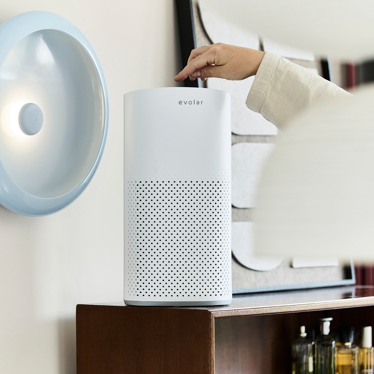 A white air purifier sits on a wooden shelf next to a blue lamp.