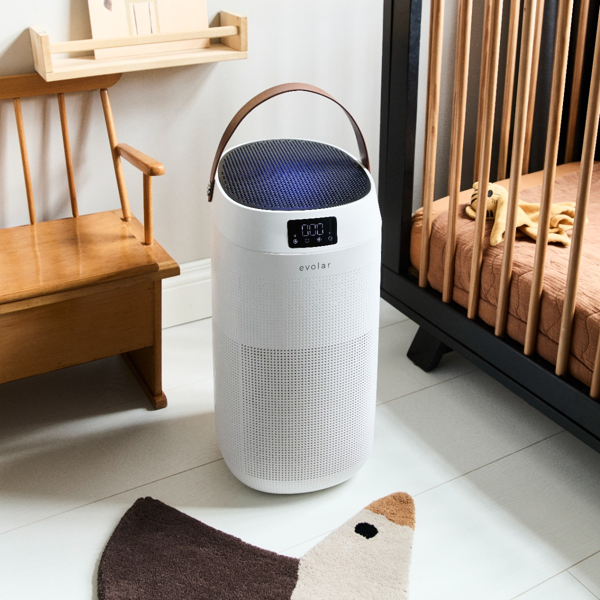 White air purifier with digital display and leather handle in a nursery with crib and wooden chair.