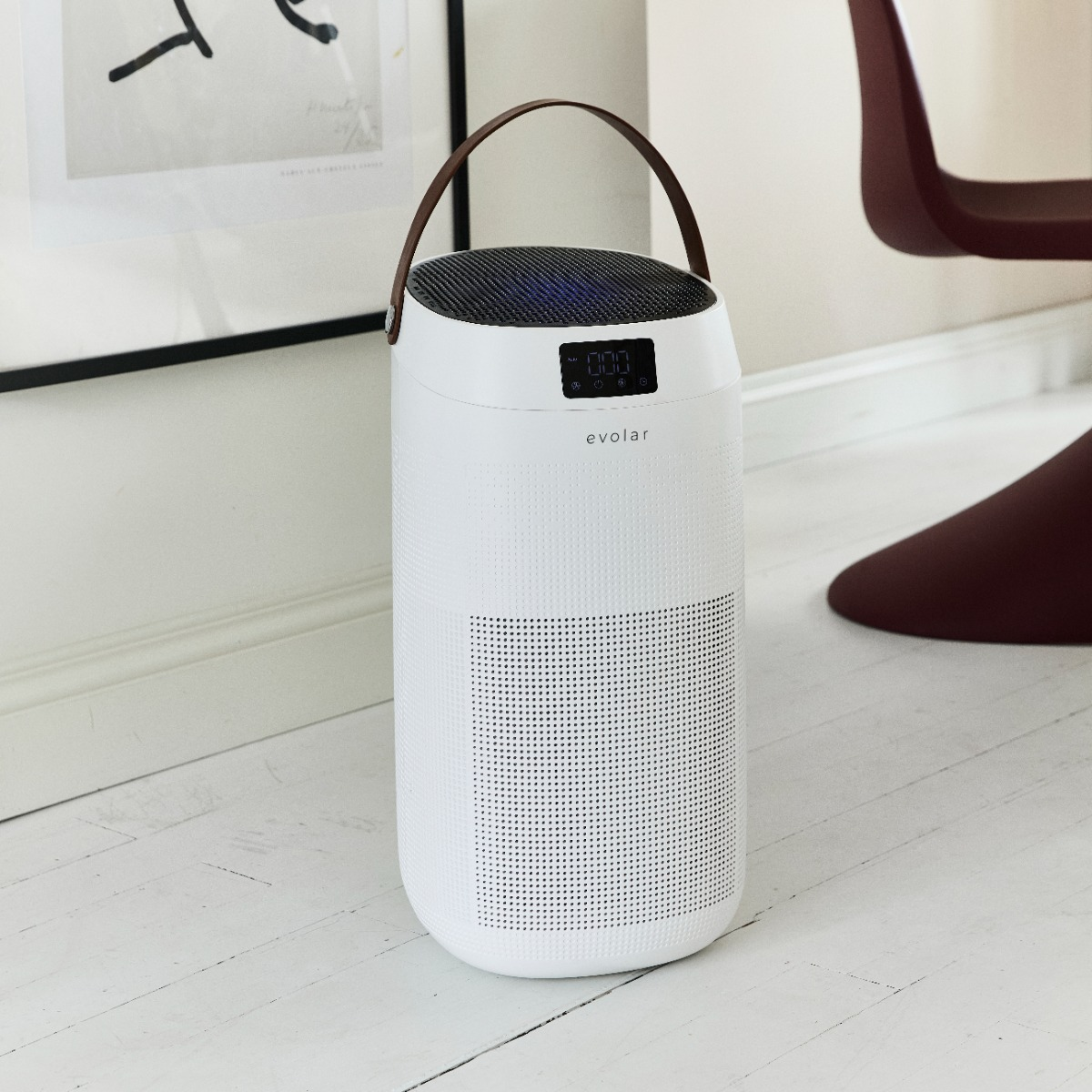 A white air purifier with a brown handle stands on a wooden floor.