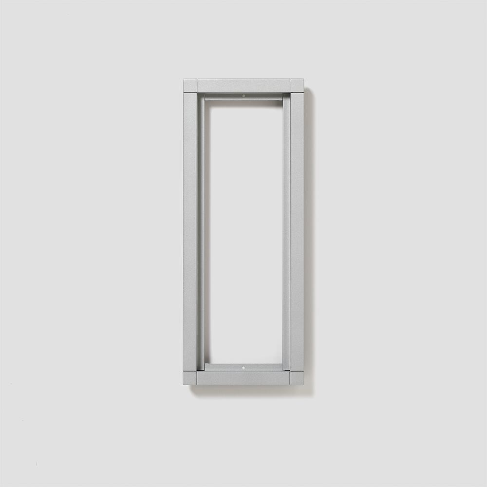 Una cornice rettangolare argentata è appesa a un muro grigio chiaro.
