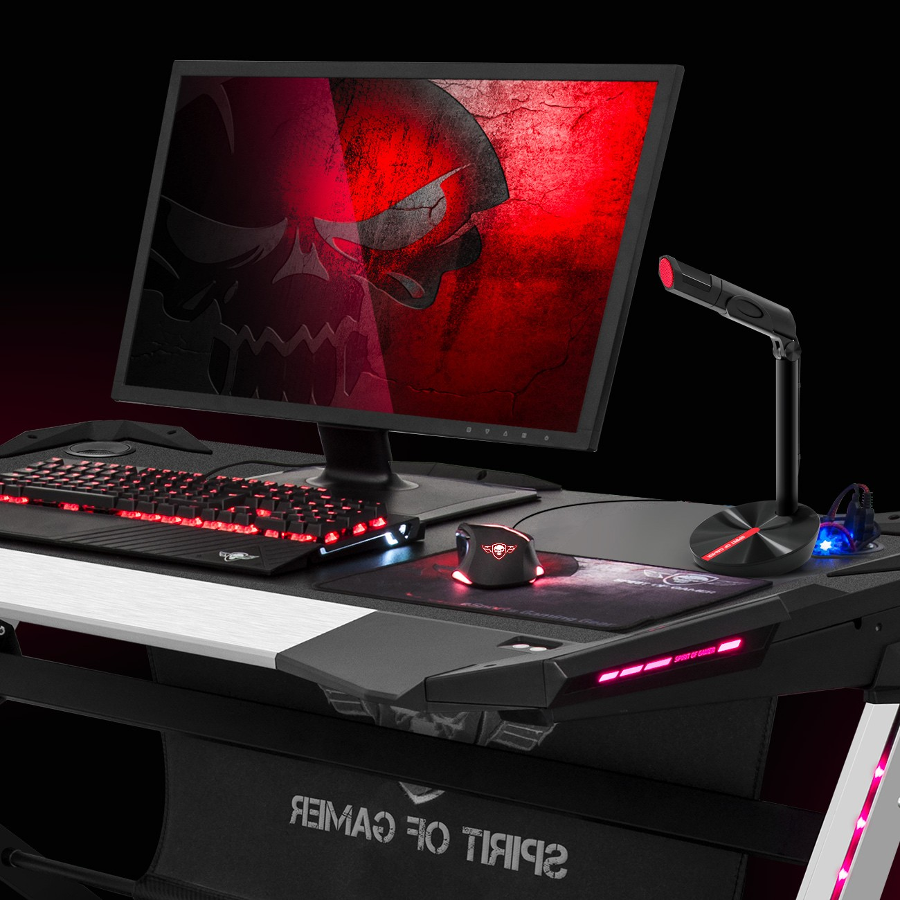 Una postazione da gaming con monitor che mostra un teschio rosso, tastiera, mouse e microfono.