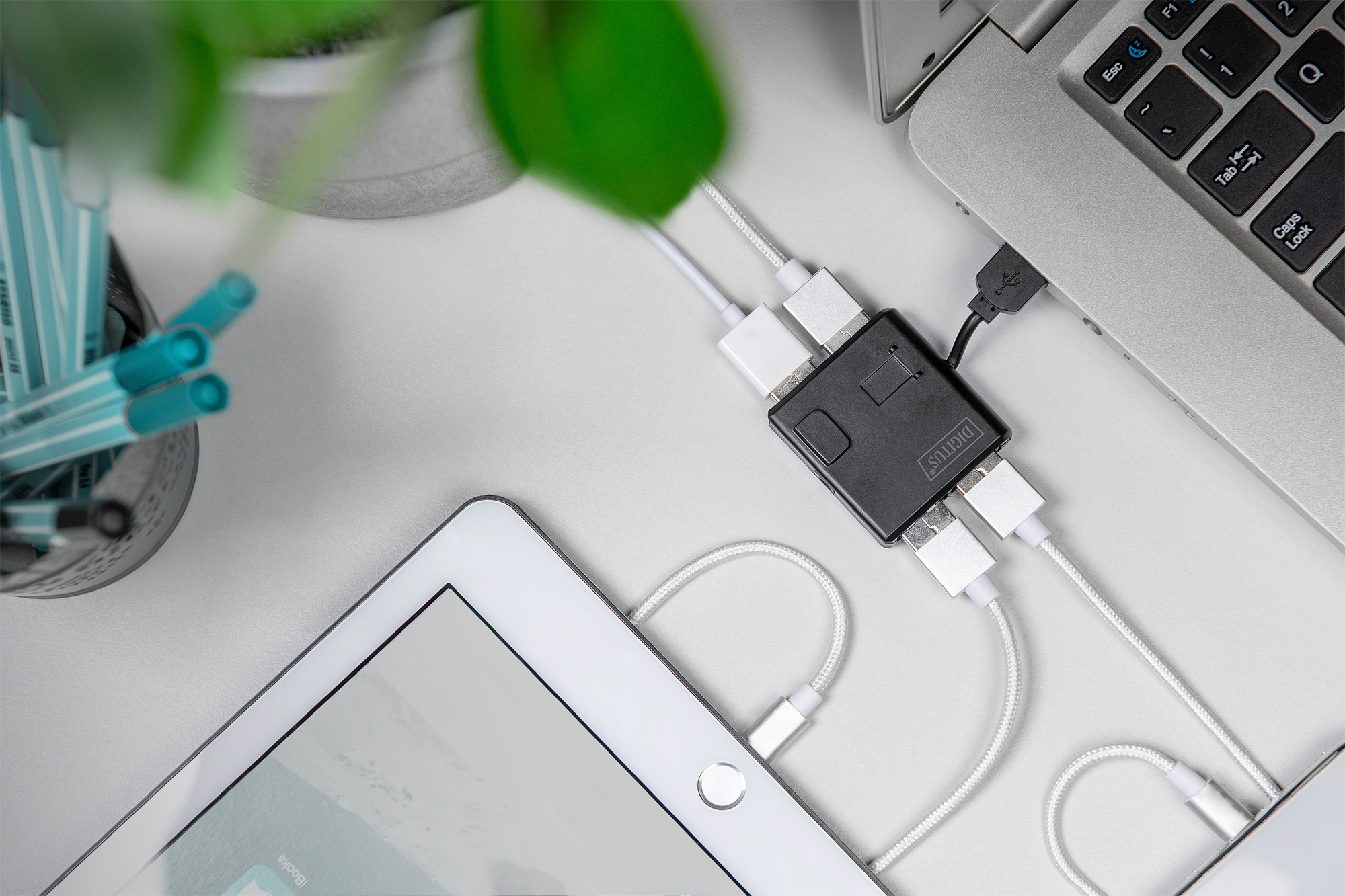 Siyah USB hub, beyaz bir masada dizüstü bilgisayar, tablet ve kalemleri bağlıyor.